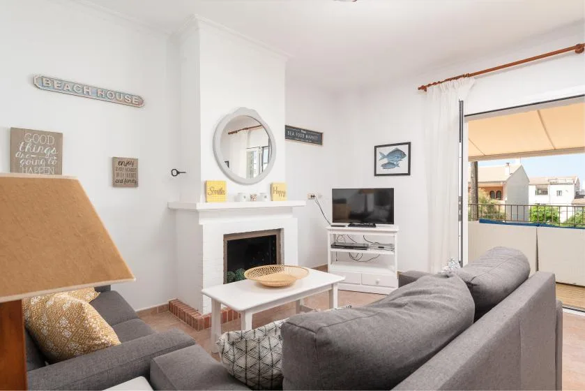 A bright living room with gray seating, a fireplace, and an open balcony doorway.