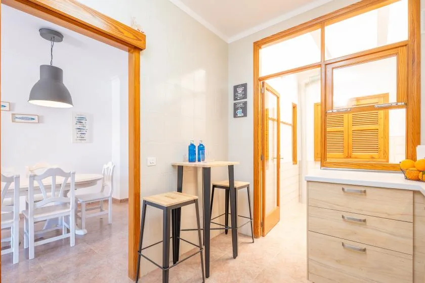 A bright dining area opens onto a small counter and a sunlit kitchen.