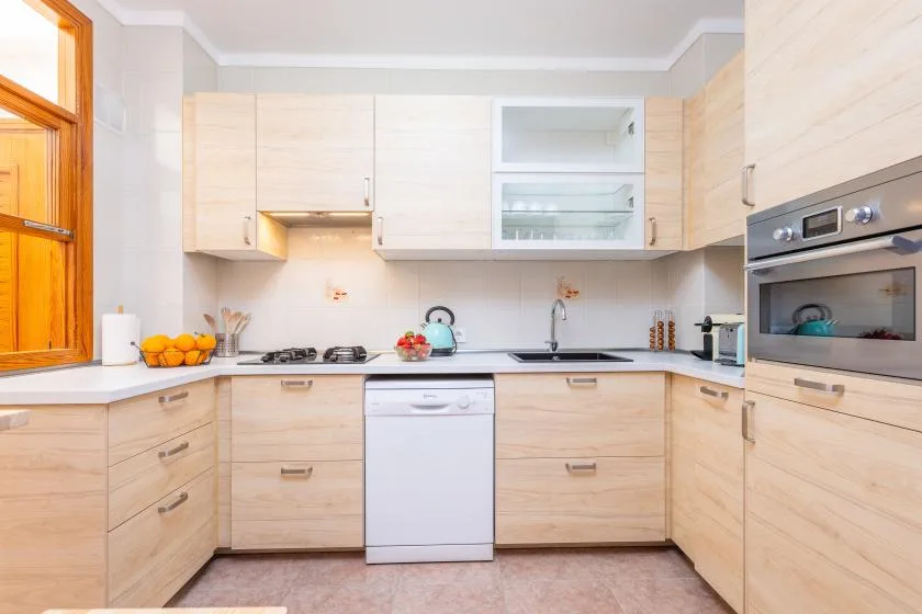 A bright kitchen with pale wood cabinets and a countertop along the walls.