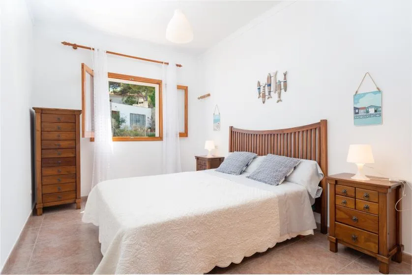A bright bedroom with a double bed, wooden furniture, and a window.