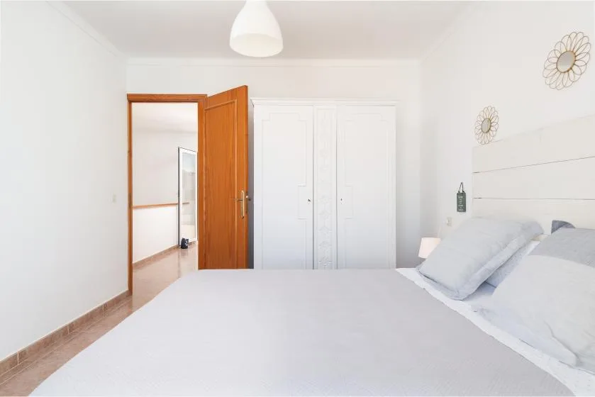 A bright bedroom with a bed, white wardrobes, and an open wooden door.