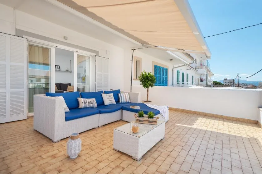 A sunny terrace with outdoor seating, a low table, and a white awning.