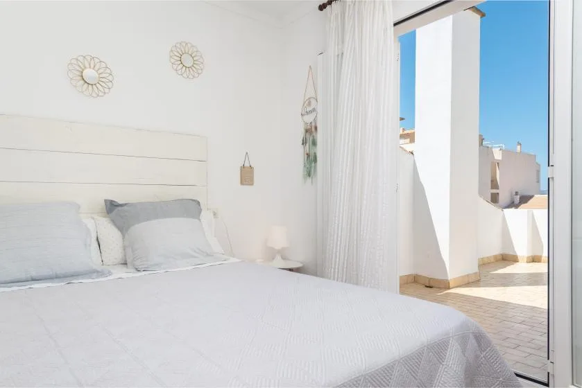 A bright bedroom with a bed beside an open glass door to a terrace.