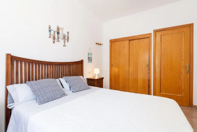 A bedroom with a wooden bed, white bedding, and built-in wooden wardrobes.