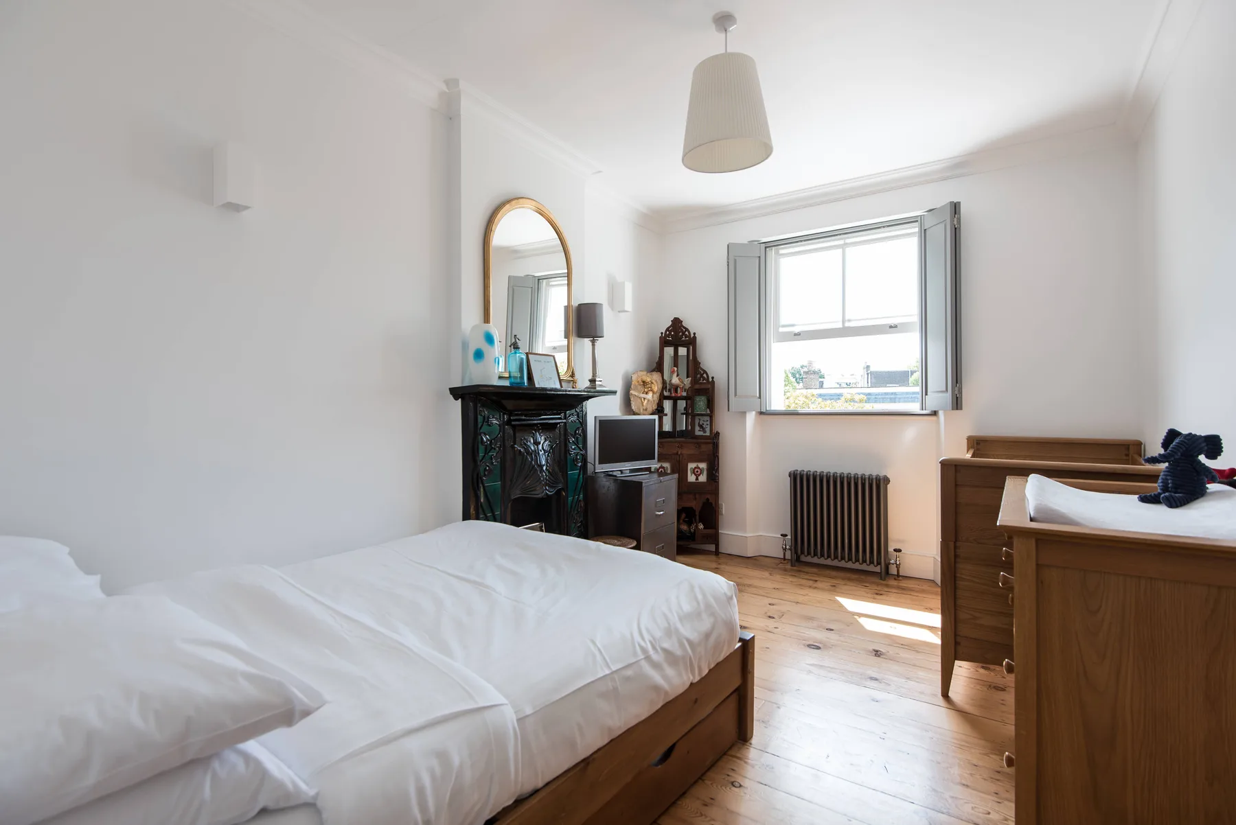 A bright bedroom with a bed, wooden flooring, and a large window.