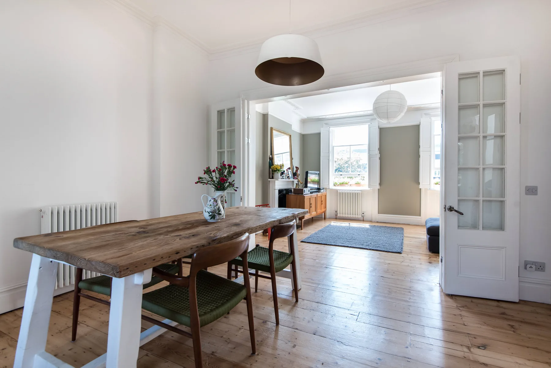 A bright dining room opens into a living area with large windows and wooden flooring.