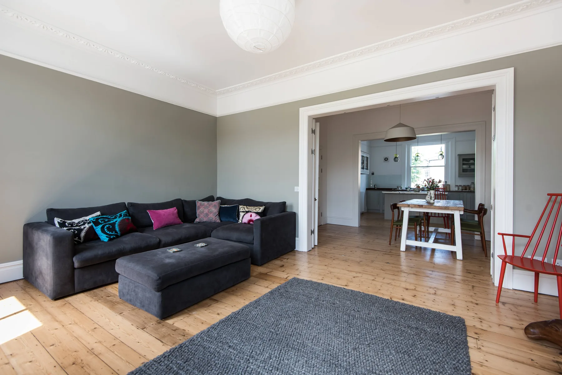 A living room with a dark sectional seating area and a view into the kitchen.