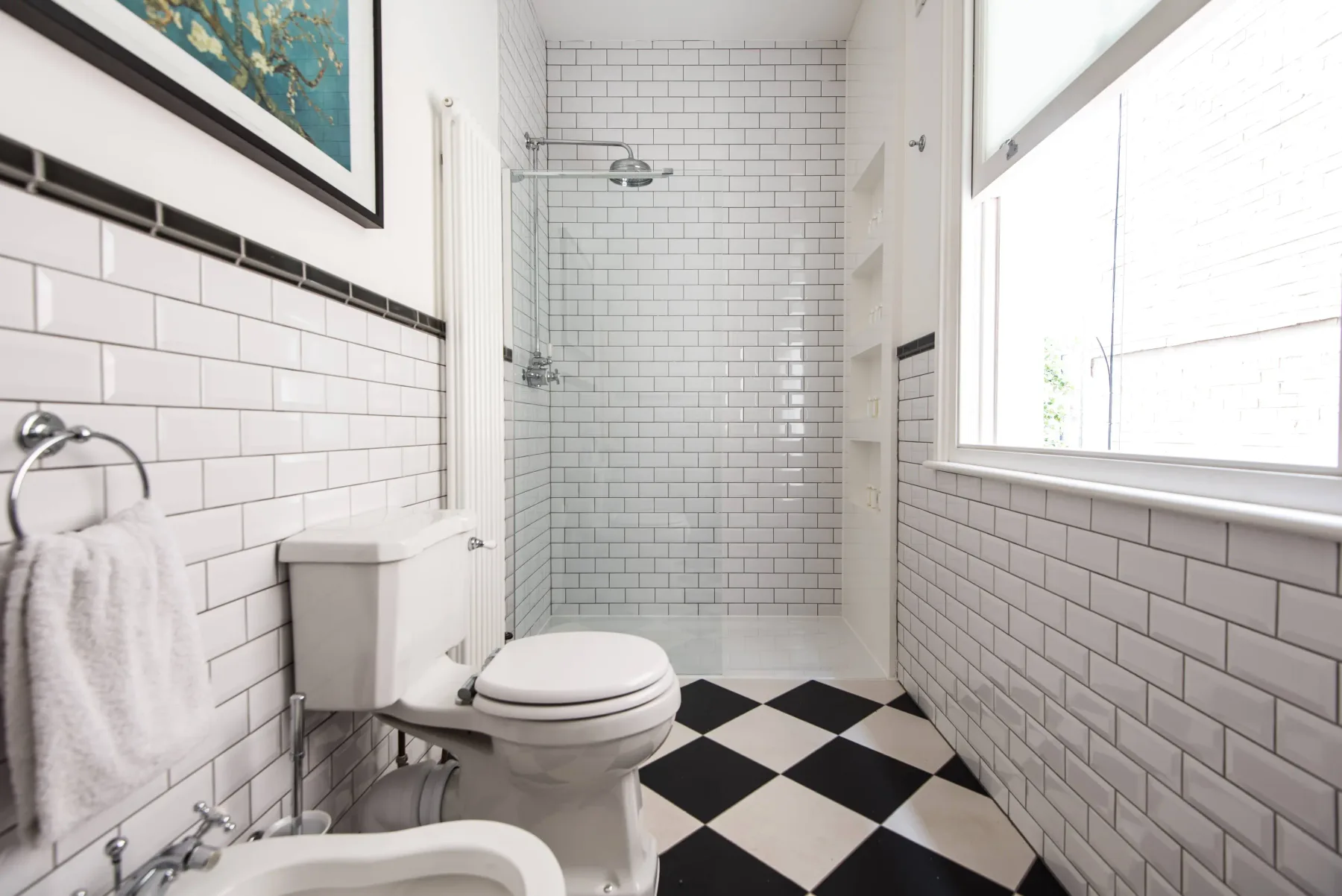 A bright bathroom with a tiled shower, toilet, and black-and-white floor.