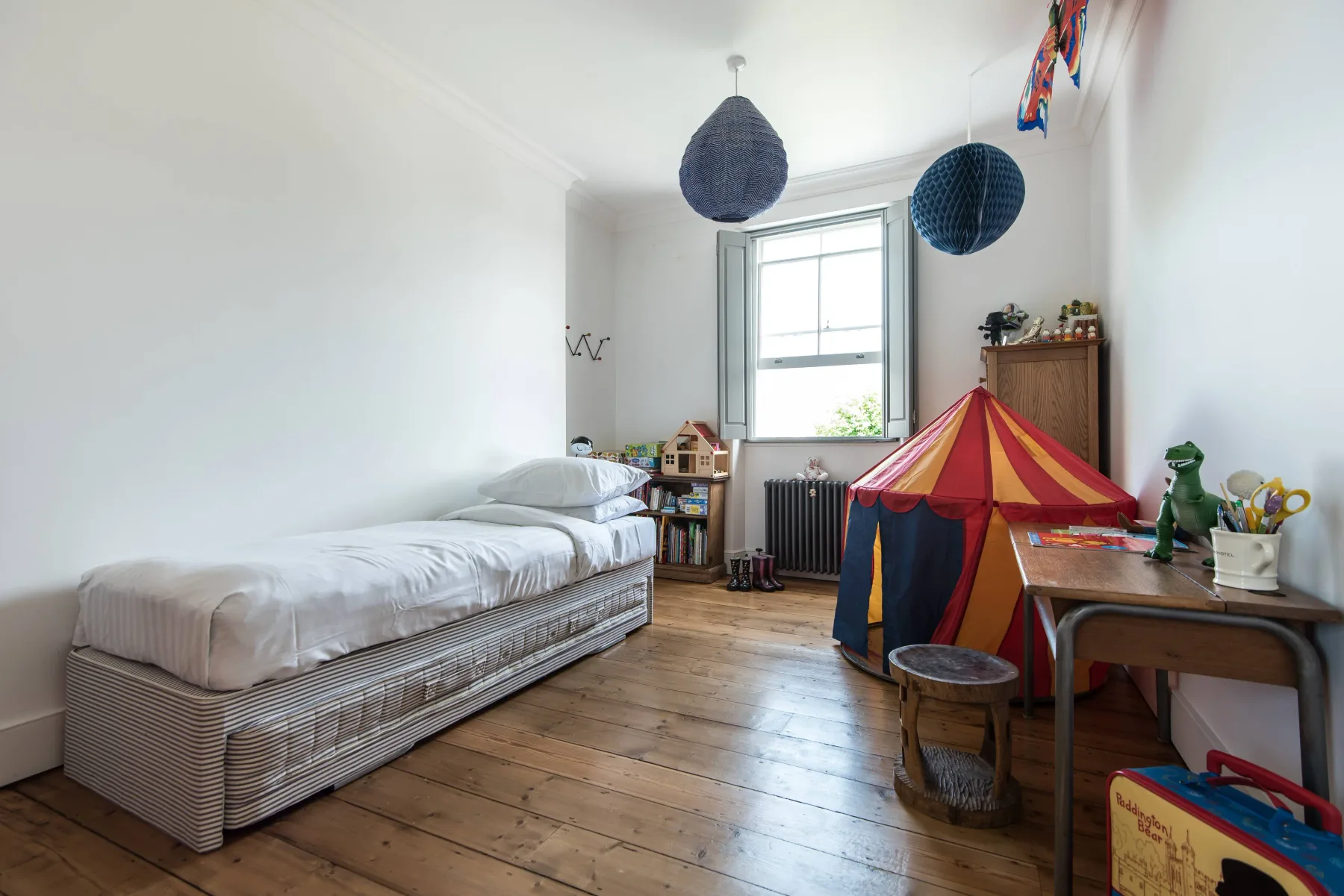 A bright bedroom with a single bed, a colorful play tent, and a desk.
