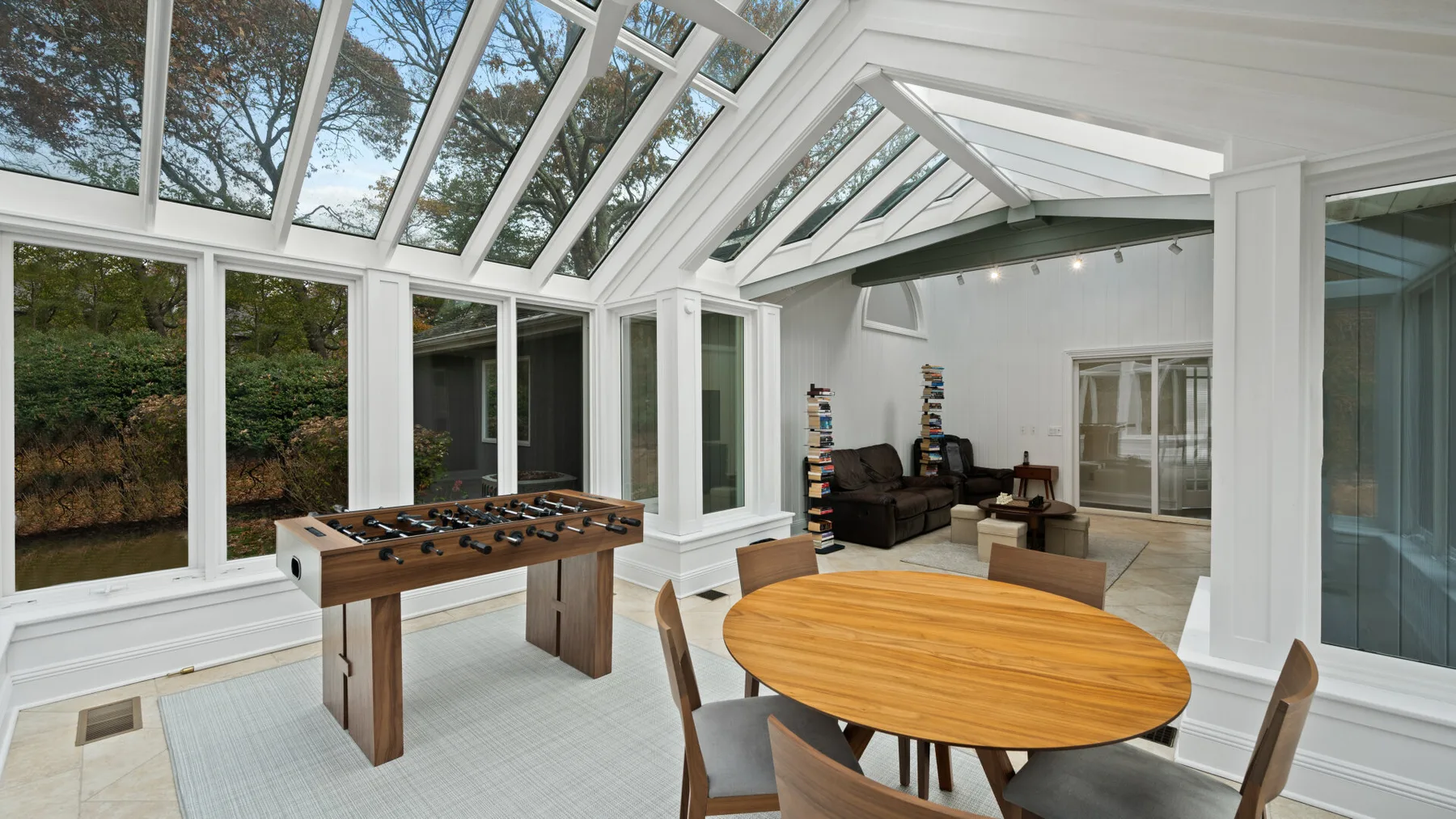 A bright glass-enclosed dining area with a round table and foosball table.