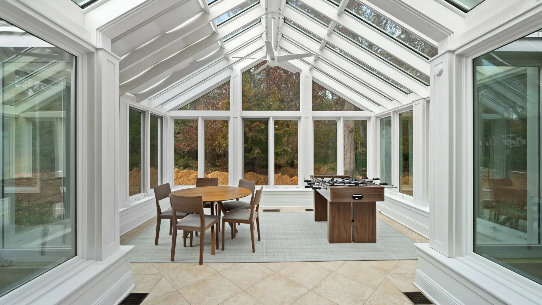 A bright conservatory with a dining table and a kitchen island beneath a glass roof.