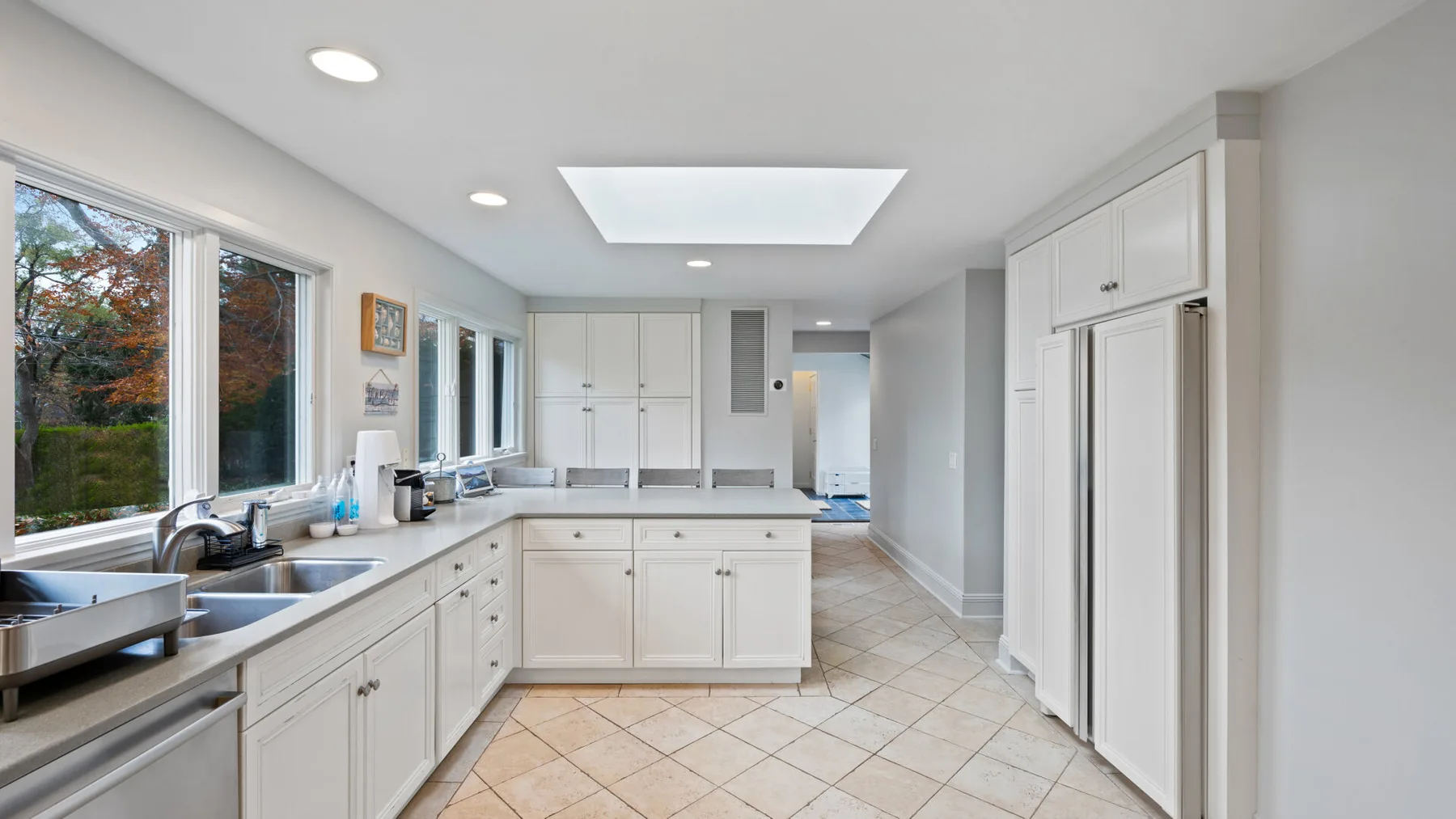 A bright kitchen with white cabinets, long countertops, and large windows.