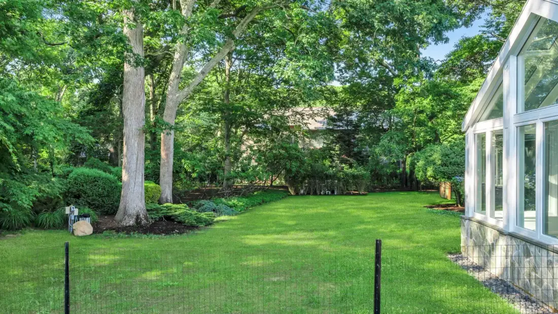 A green lawn bordered by mature trees beside a glass-walled building.