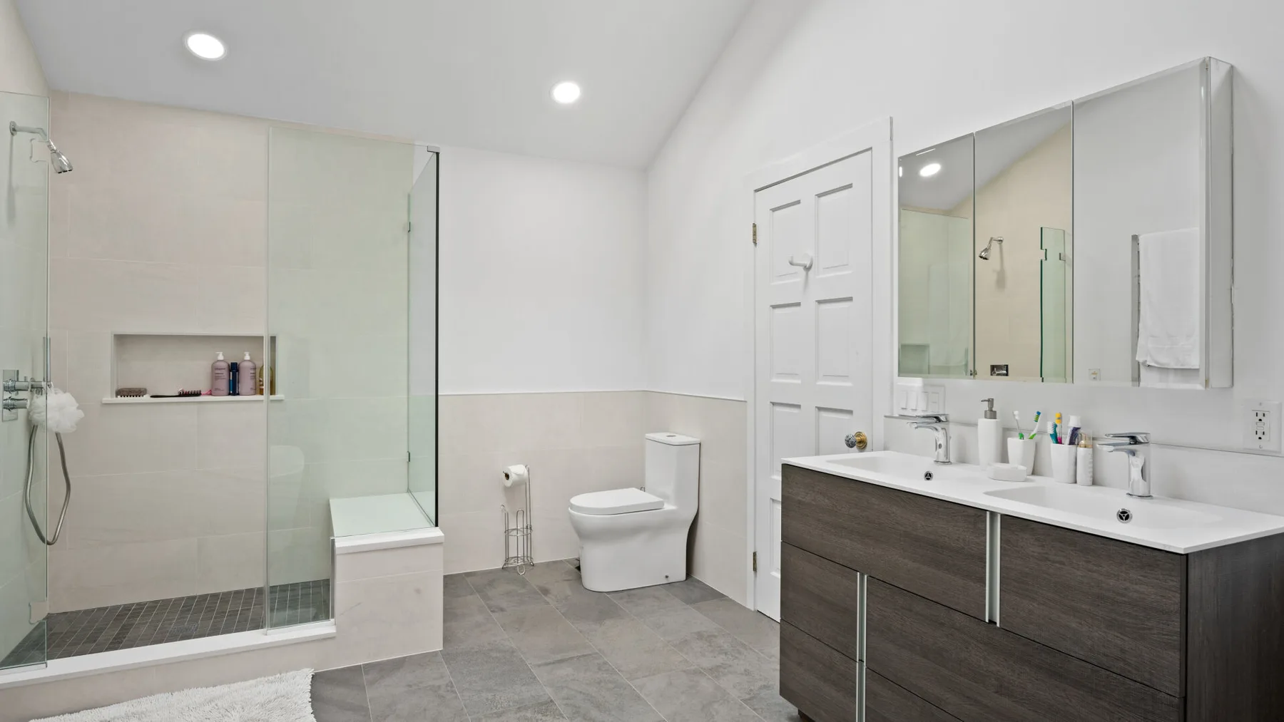 A bright bathroom with a glass shower, toilet, and double vanity.