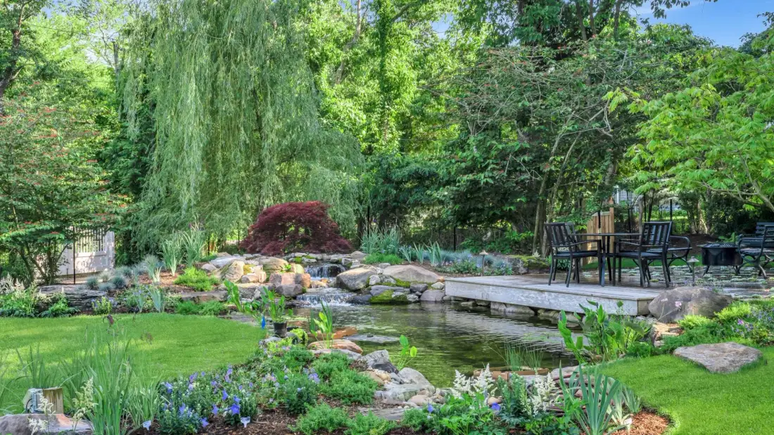 A landscaped garden with a small pond, stone edging, and outdoor seating.
