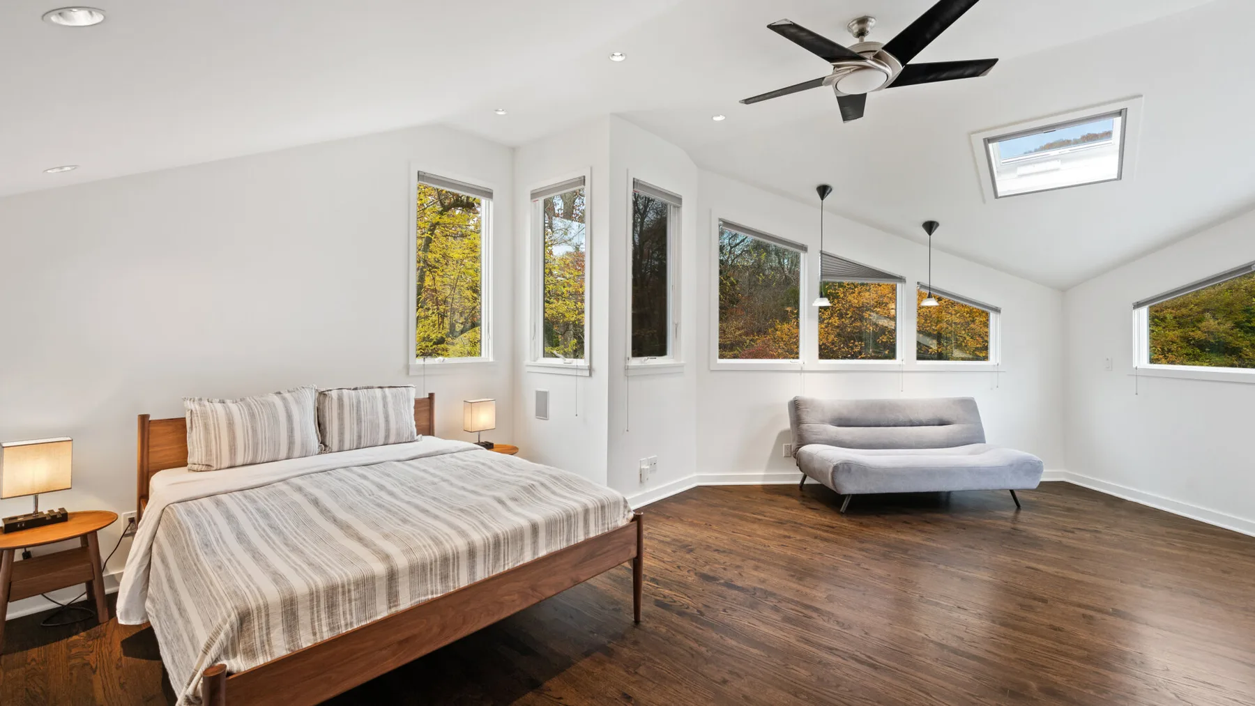 A bright bedroom with a bed and seating beneath large windows.