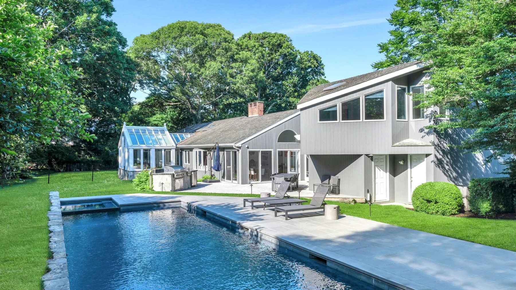 Una casa moderna da a una piscina, con árboles y césped alrededor del patio.