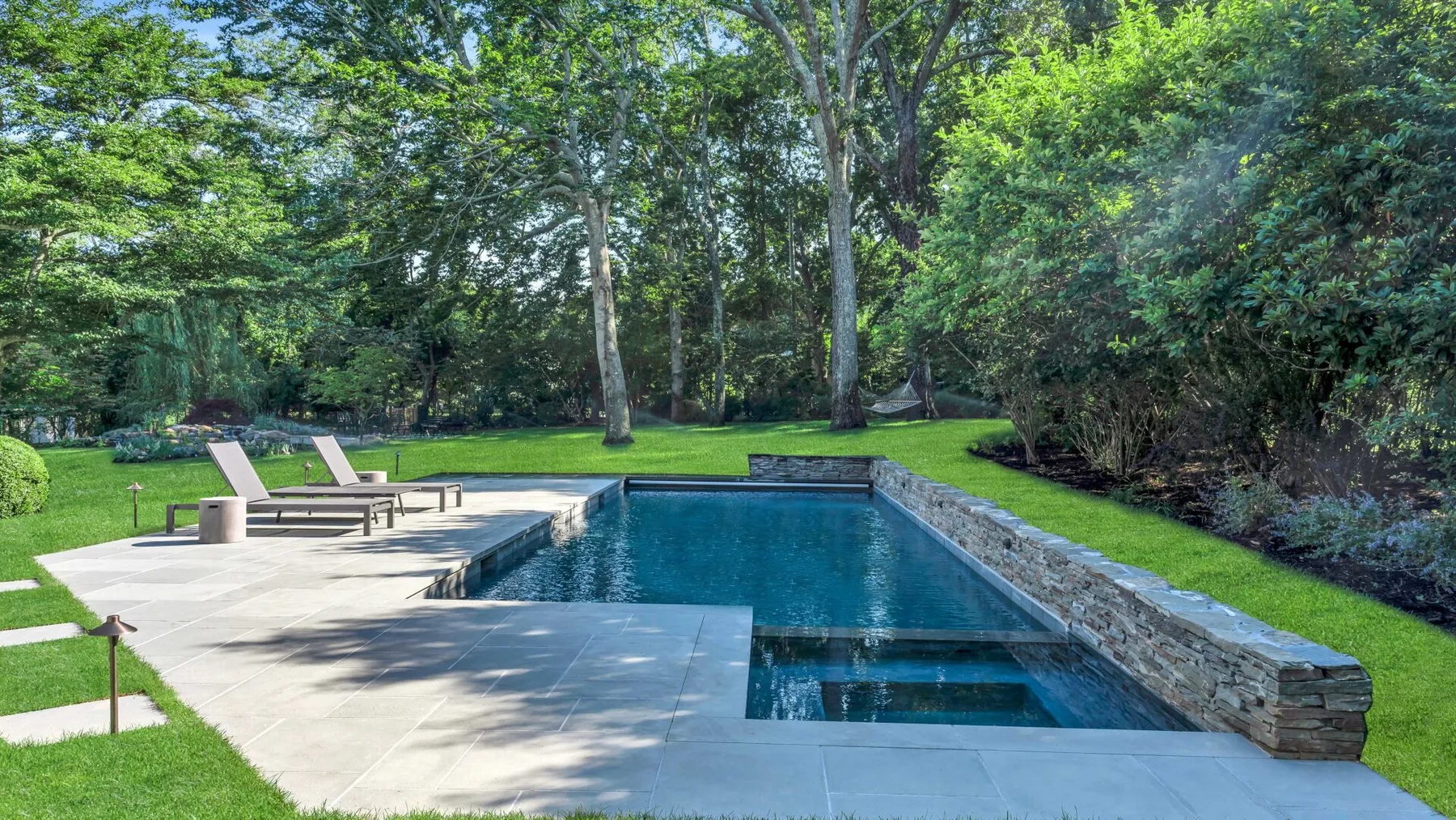 Una piscina al aire libre está junto a un patio pavimentado y un césped verde.