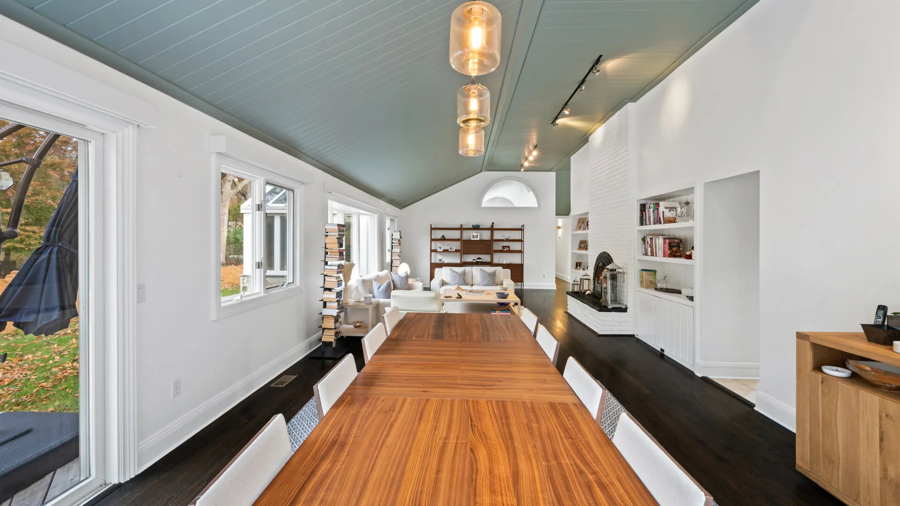 A bright dining area with a long wooden table, windows, and built-in shelving.