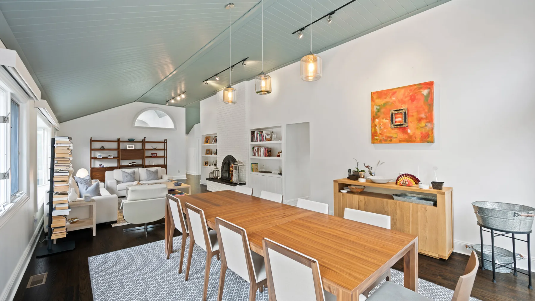 A bright dining and living area features a long wooden table and built-in bookshelves.