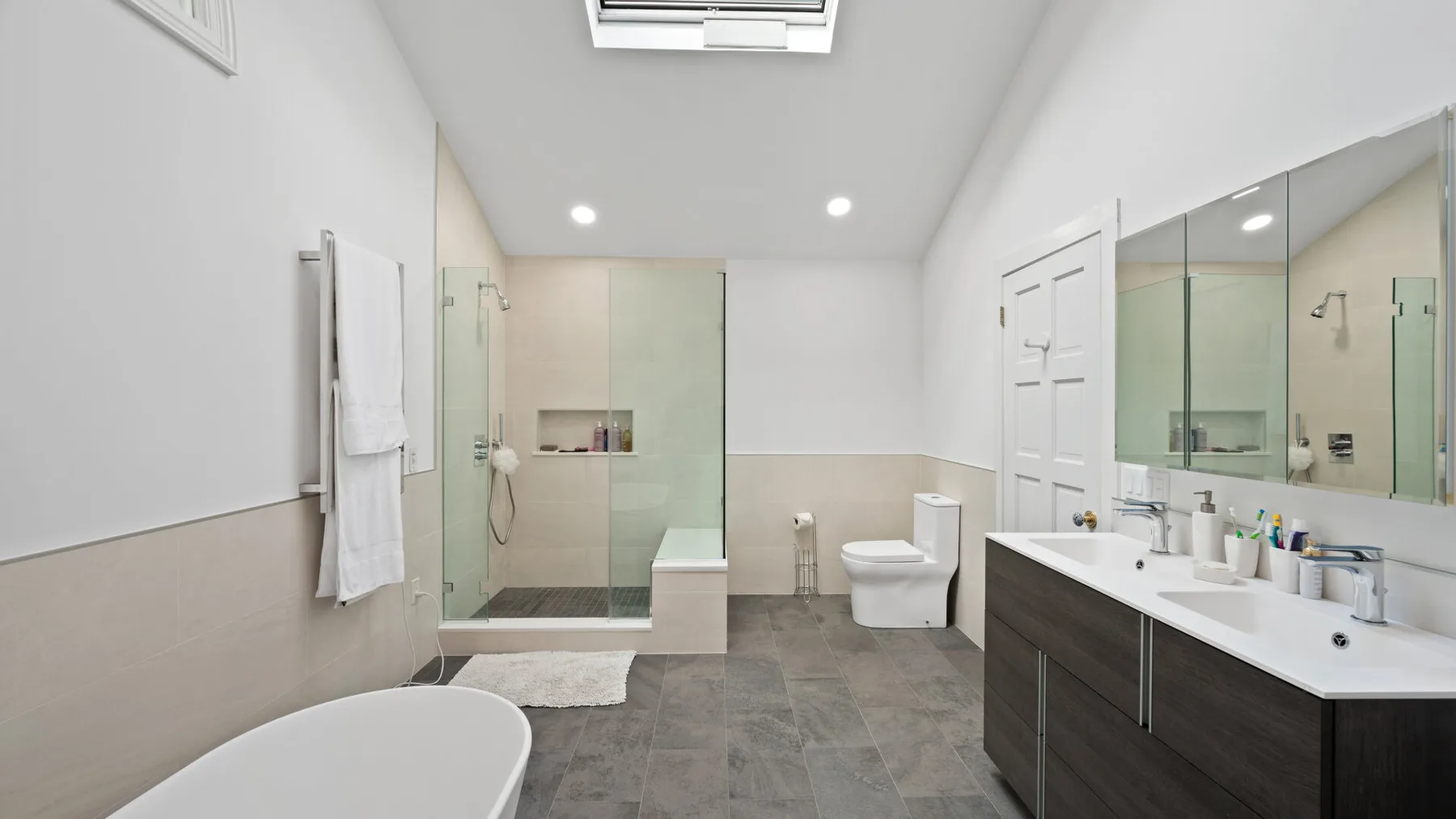 A bright bathroom with a glass shower, bathtub, and double sink vanity.