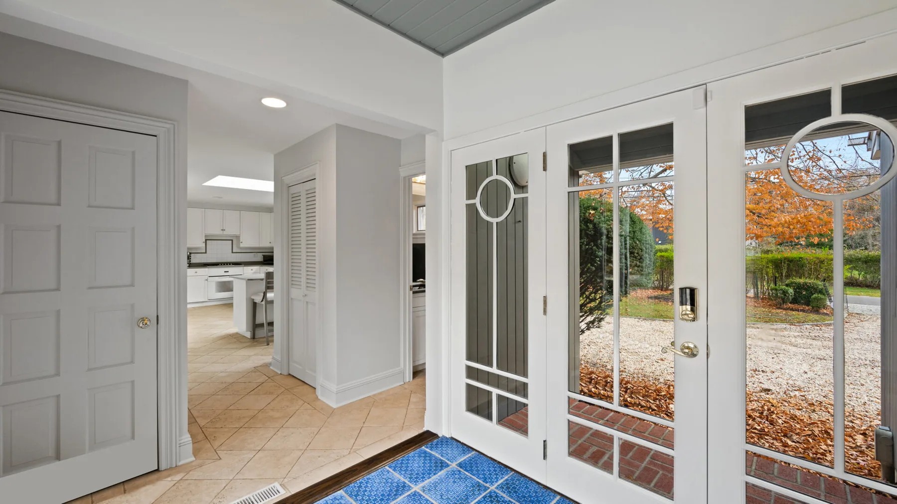 A bright entryway with glass-paneled doors opening onto a leafy outdoor view.
