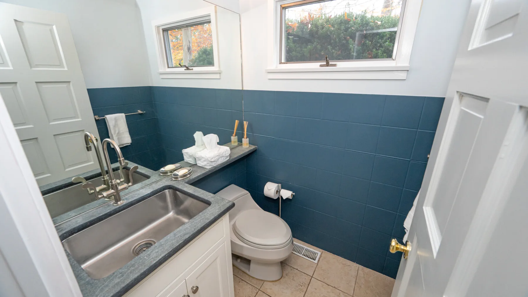 A bathroom with a double sink, toilet, and blue tiled walls.
