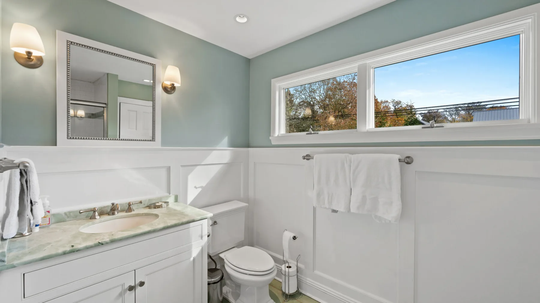 A bathroom with a vanity, toilet, and wide window.