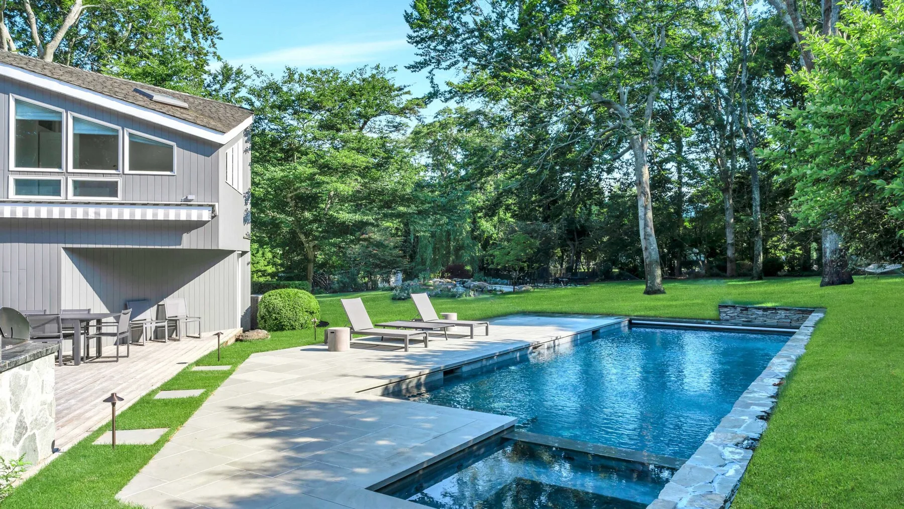 An outdoor swimming pool beside a house, patio, and green lawn.
