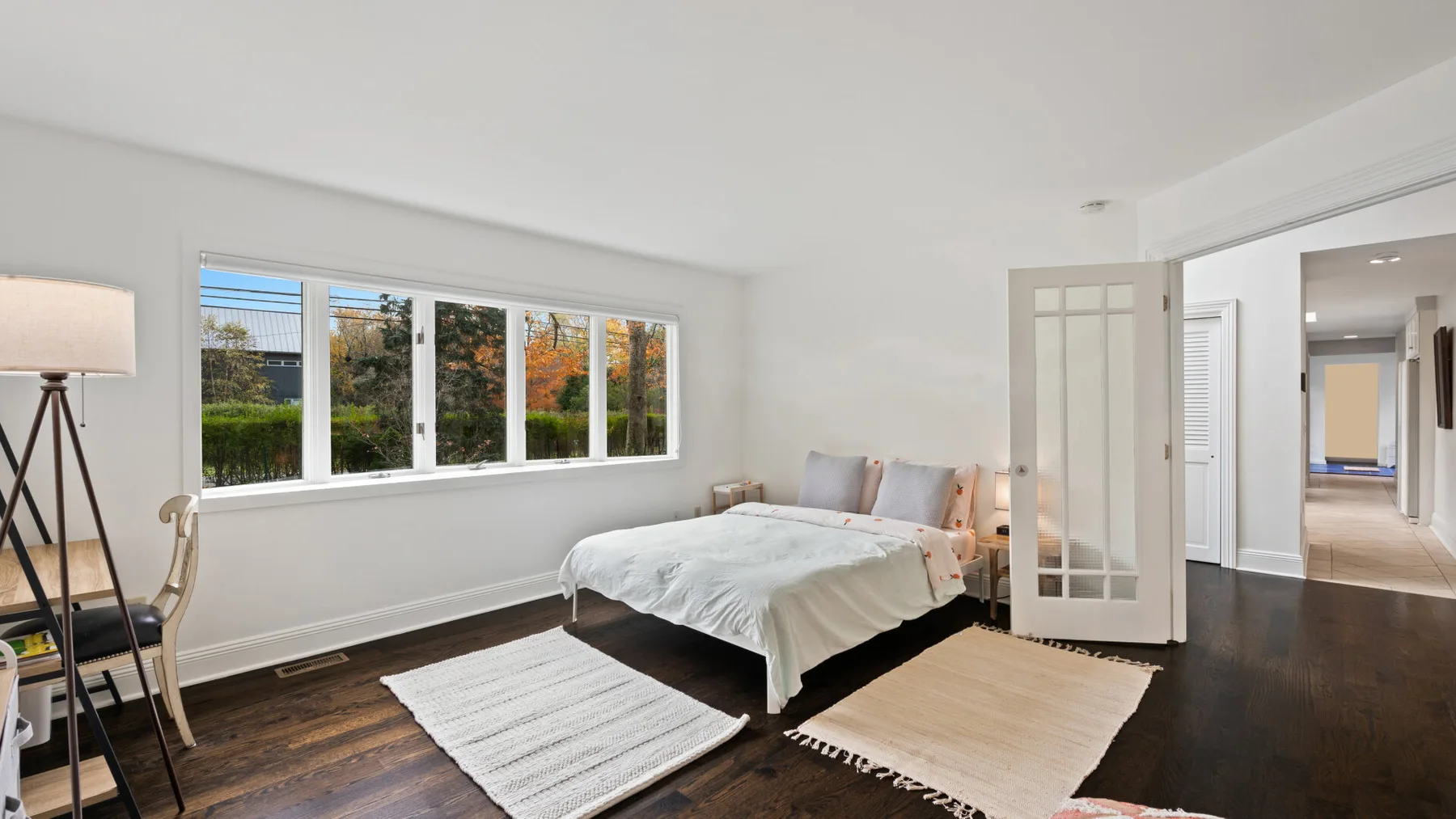 A bright bedroom with a bed beside a wide window and light-colored rugs.