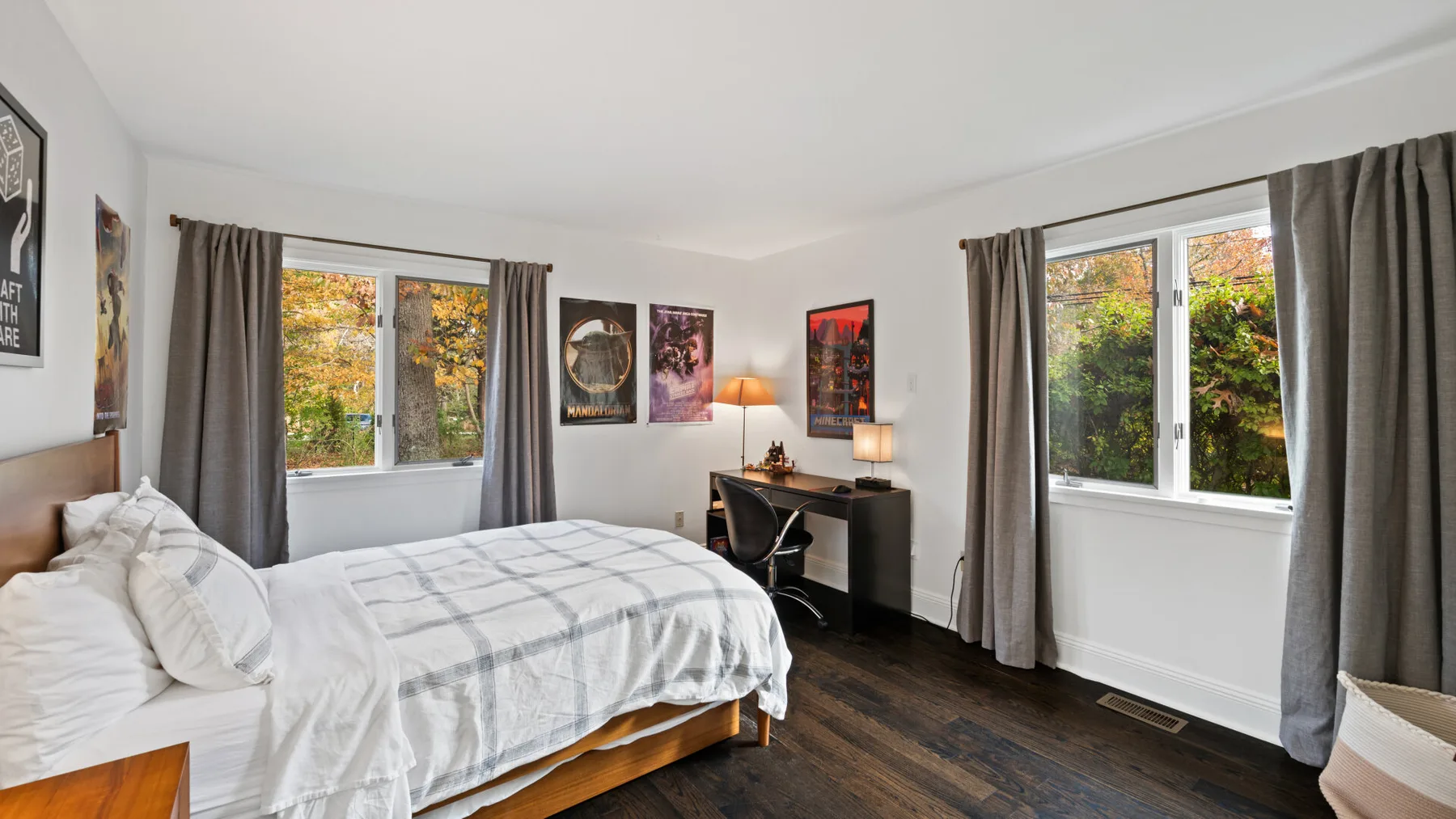 A bright bedroom with a bed, desk, and windows overlooking greenery.
