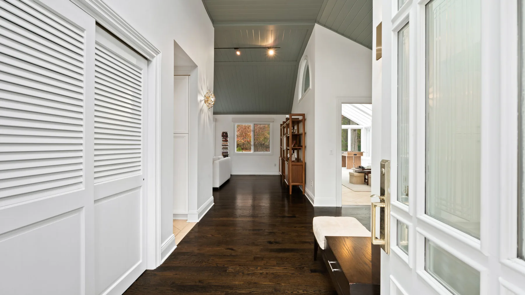 A long interior hallway with dark wood flooring, white doors, and a bench.