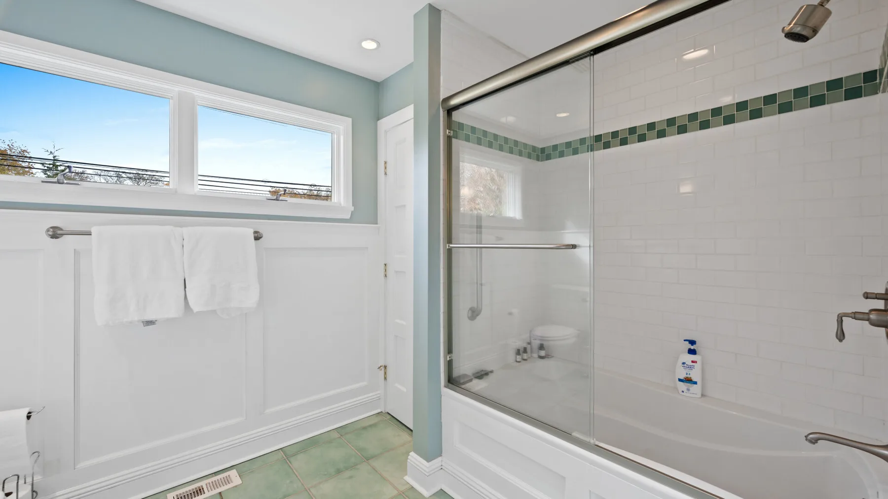 A bright bathroom features a glass shower and a wide window.