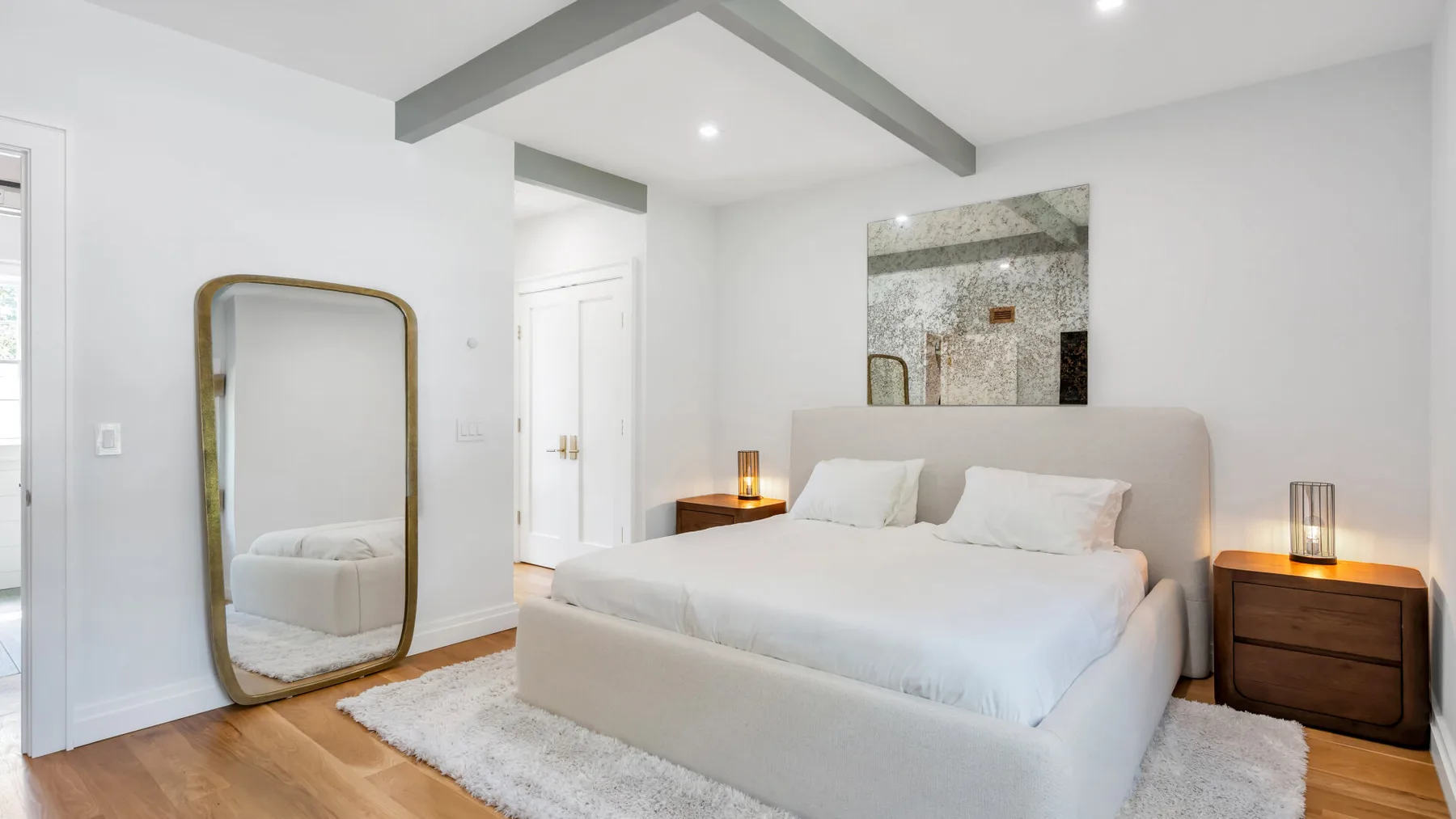 A bright bedroom with a large bed, bedside tables, and a leaning mirror.