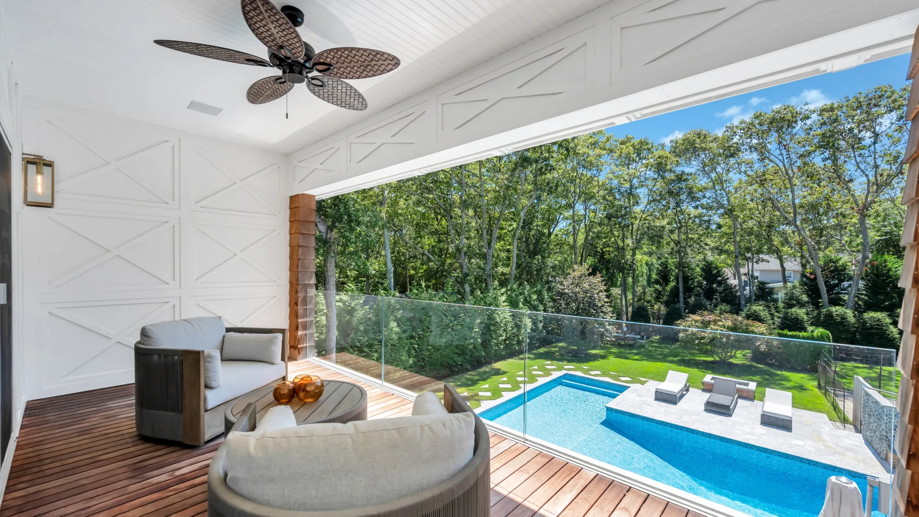 A bright covered patio overlooks a swimming pool and tree-lined yard.