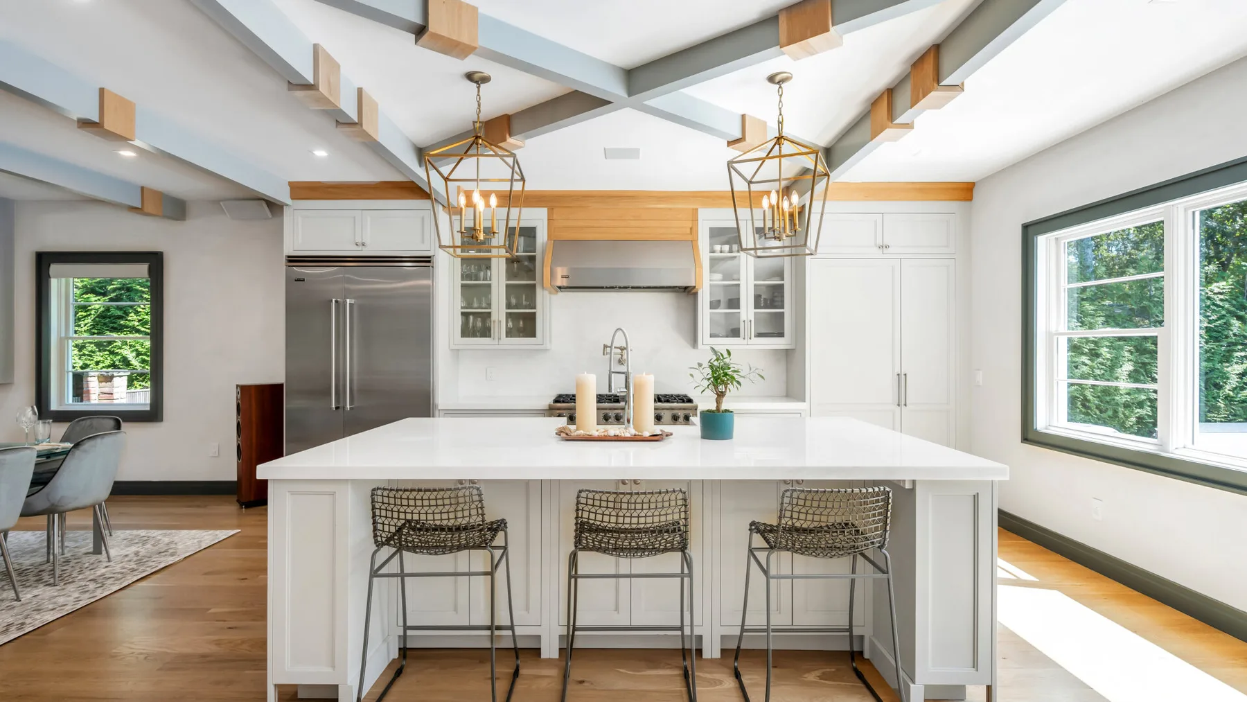 A bright kitchen with a large island, three stools, and windows.
