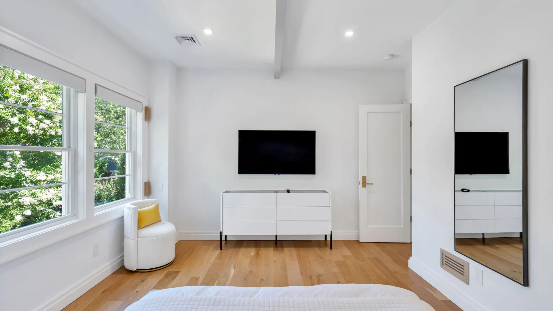 A bright living room with a wall-mounted television and large windows.