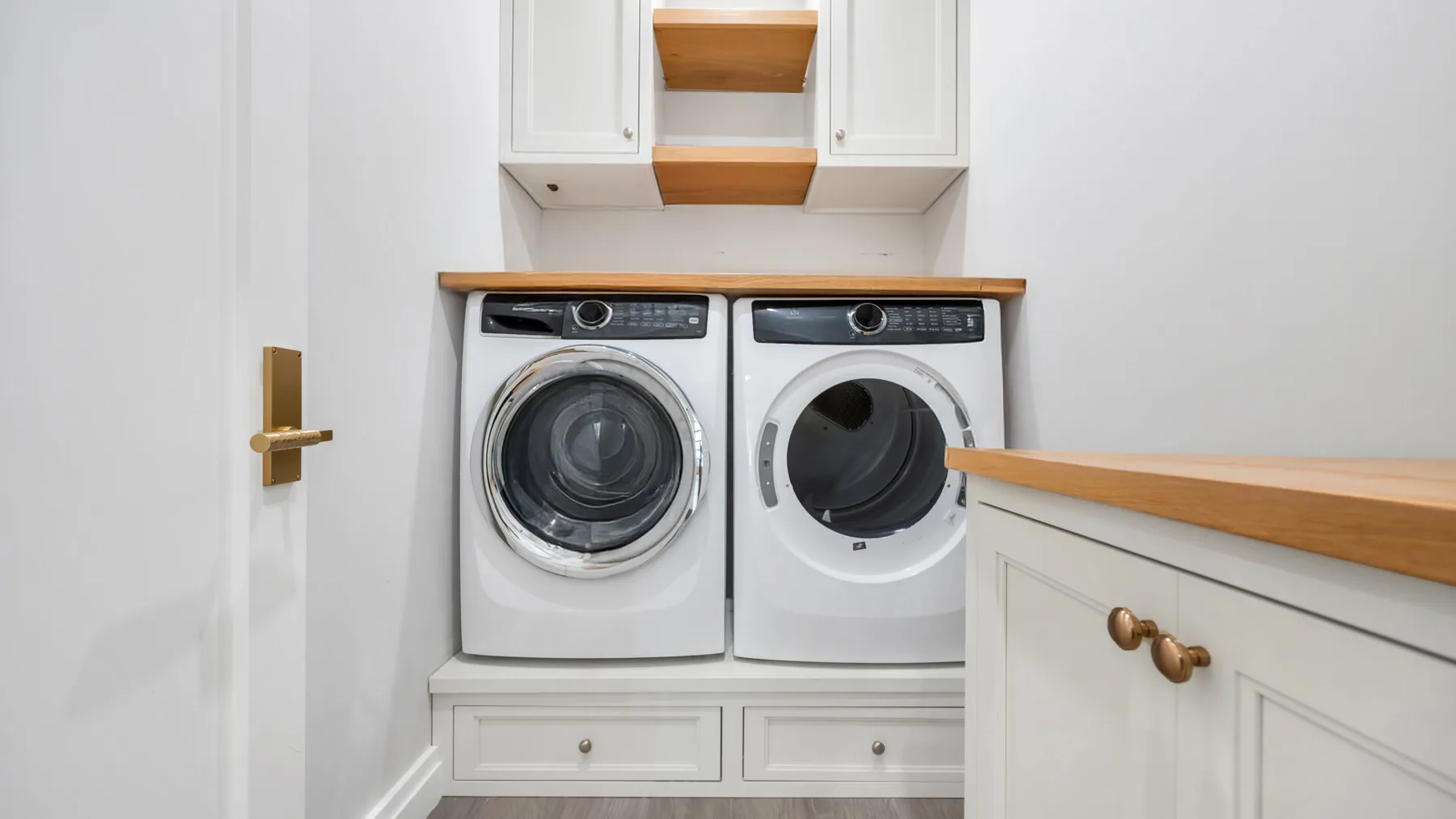 A laundry area with two front-loading machines beneath white cabinets.