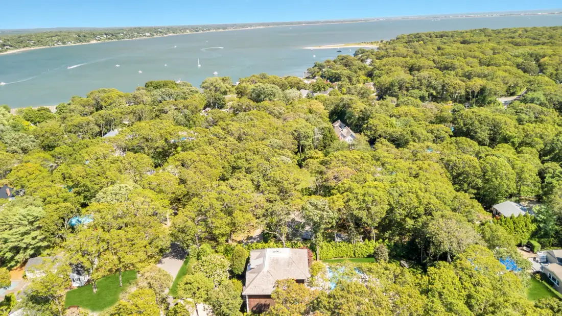 An aerial view of tree-covered homes beside a broad coastal inlet.