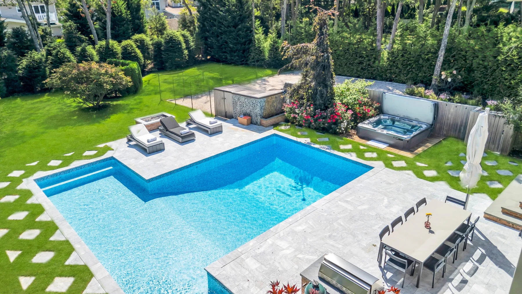 An outdoor swimming pool sits beside a patio with dining seating and a hot tub.