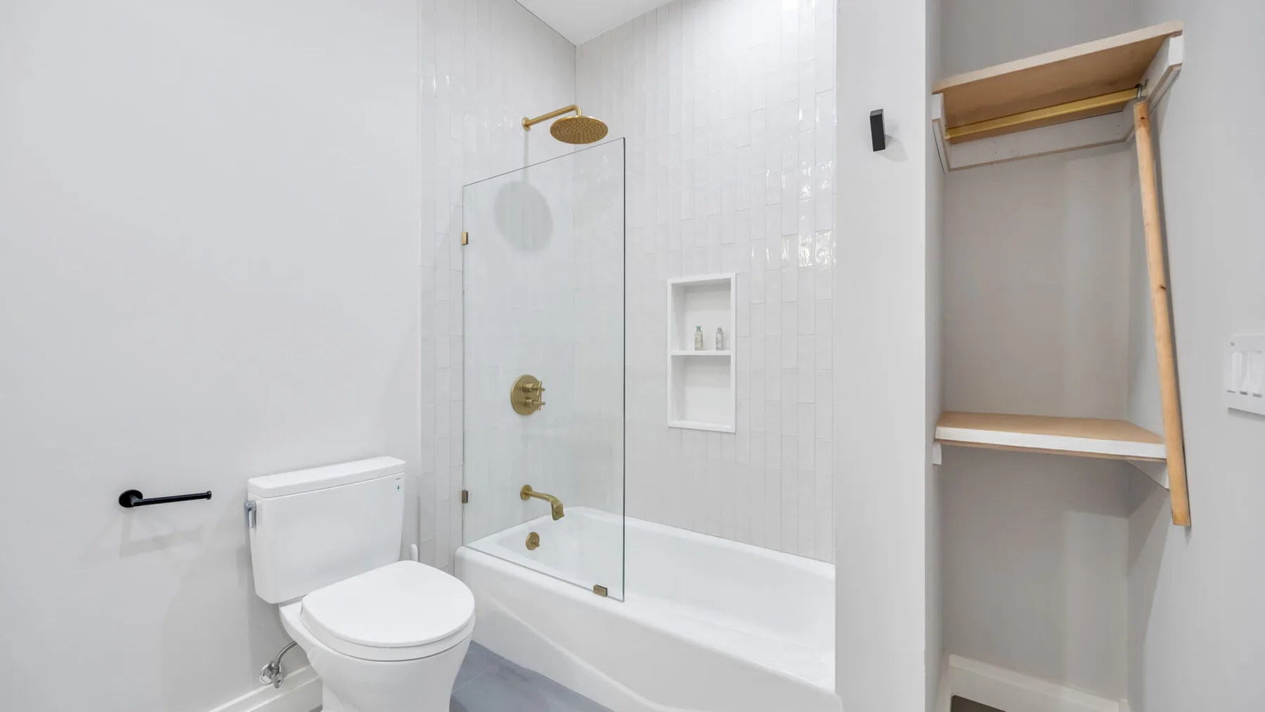 A bright bathroom with a bathtub, glass shower screen, and toilet.