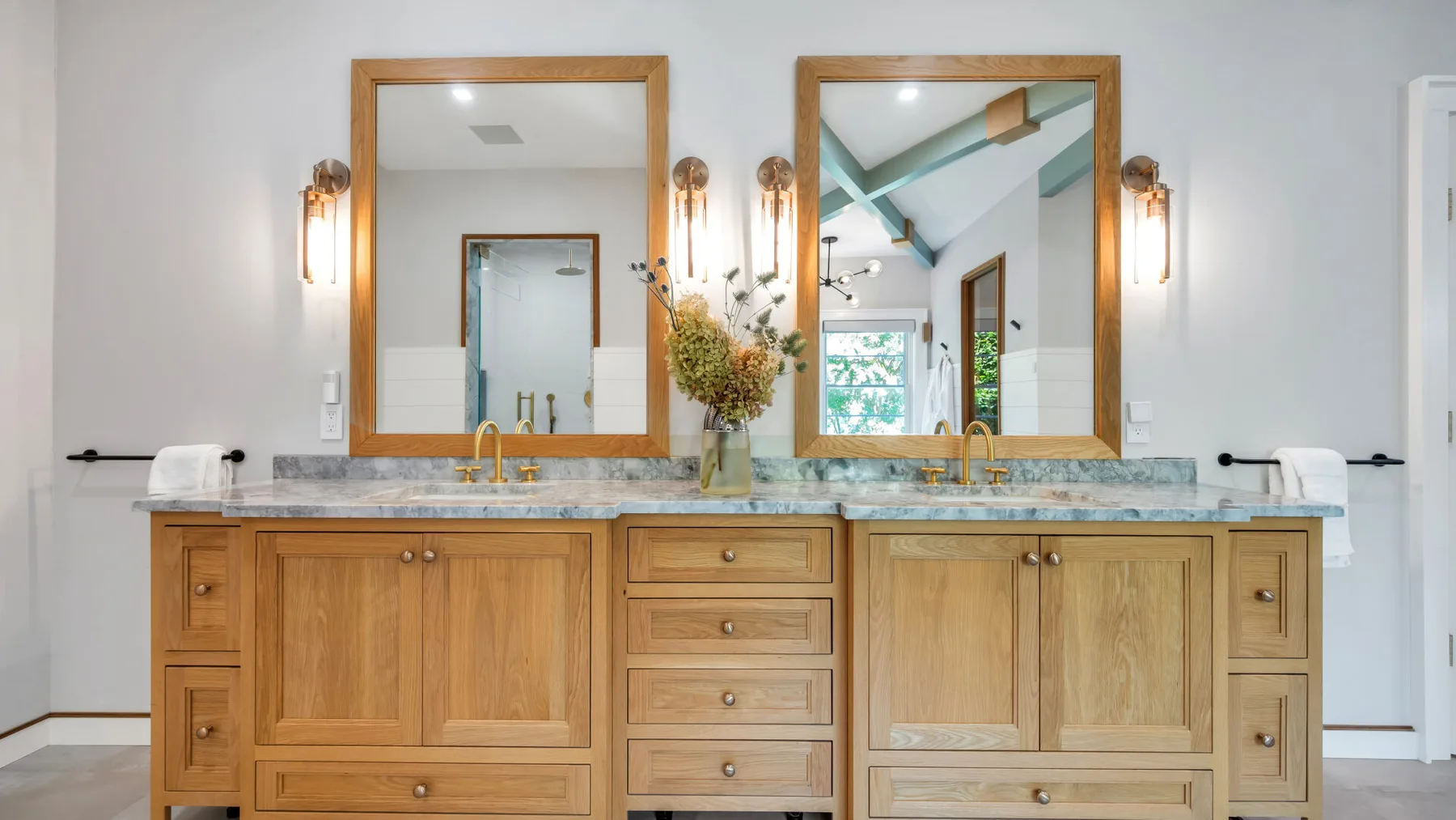 A bathroom vanity with a stone countertop, wooden cabinets, and two mirrors.