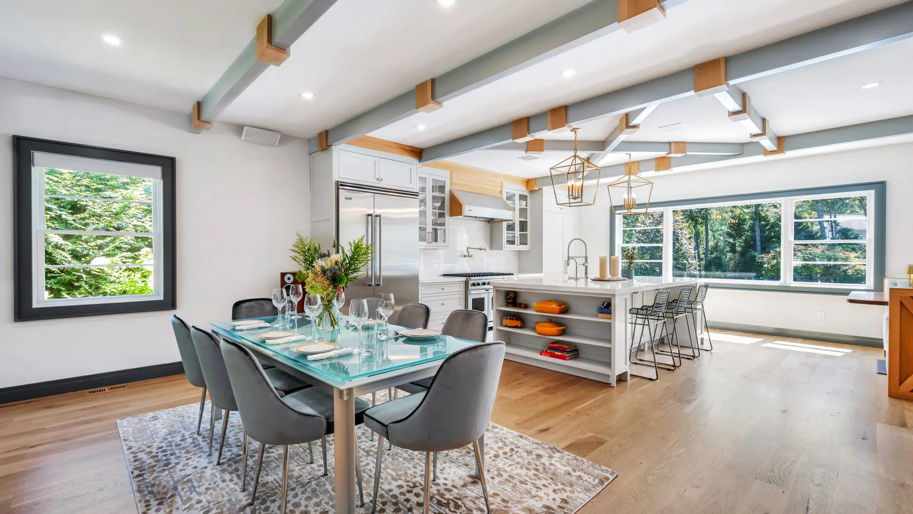 A bright open-plan kitchen and dining area with large windows and a glass dining table.