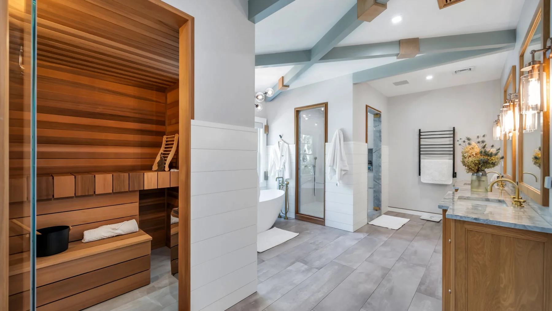 A bright bathroom with a glass shower, bathtub, and wood-paneled sauna.