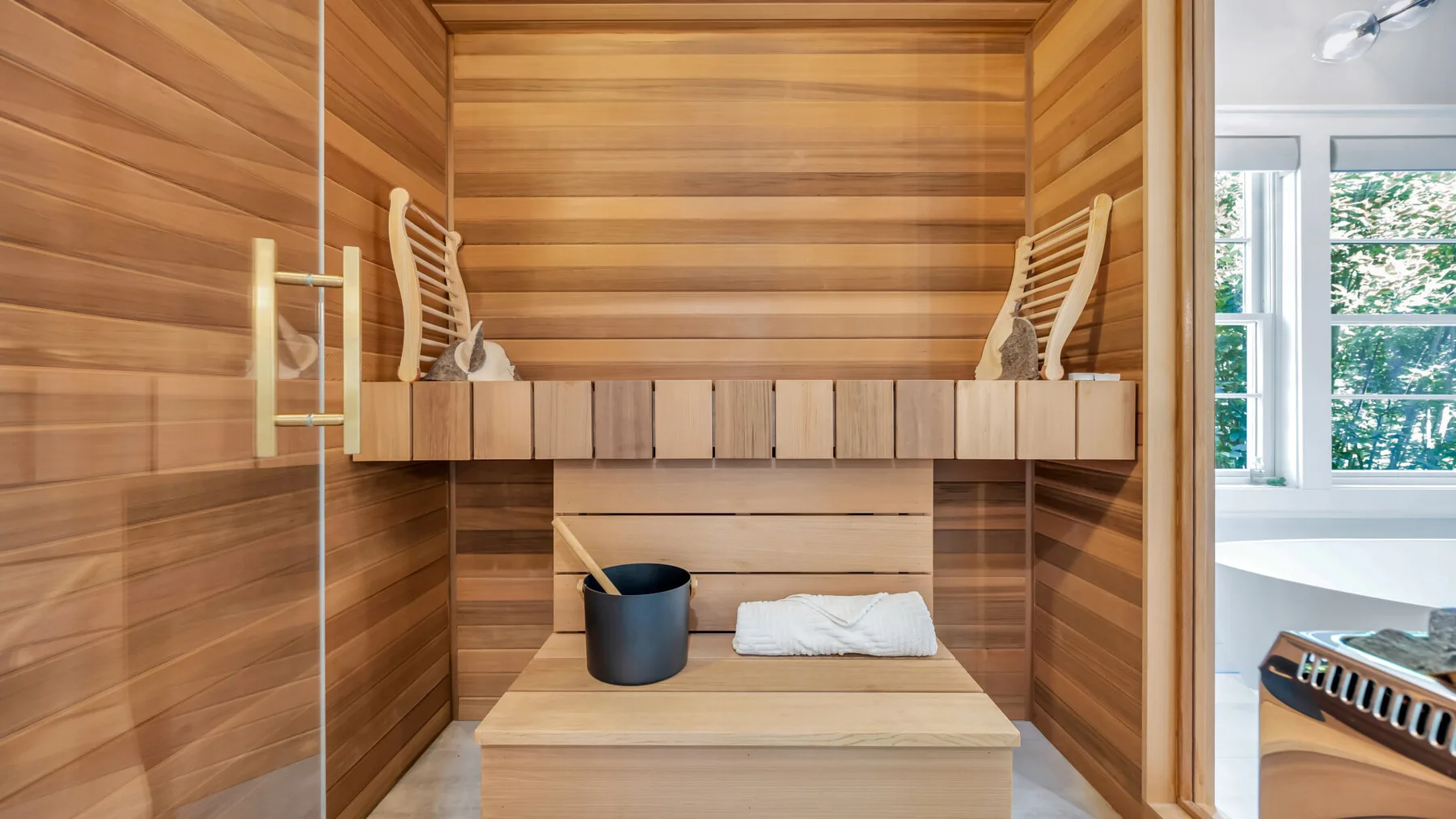 A wood-paneled sauna room with a bench, bucket, and folded towel.