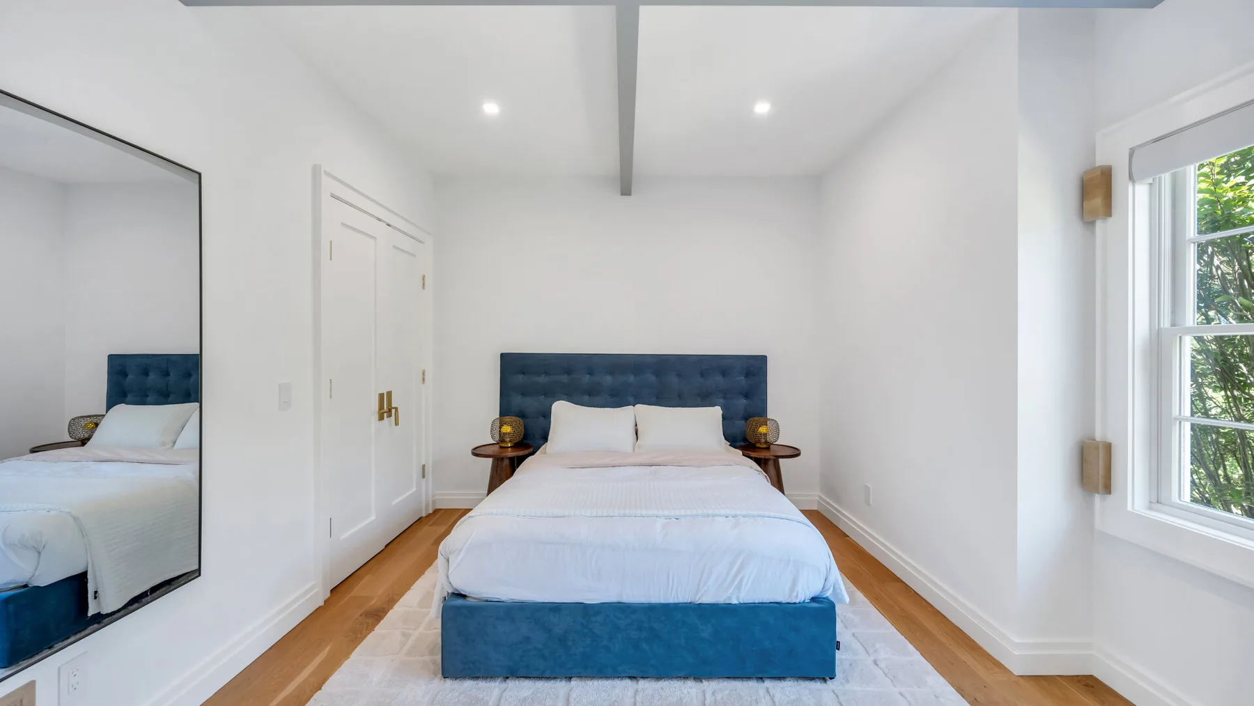 A bright bedroom with a bed between two bedside tables and a large mirror.
