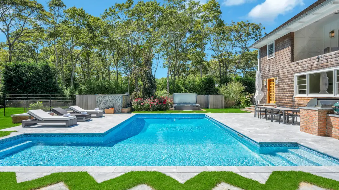 An outdoor swimming pool sits beside a paved patio and a house.