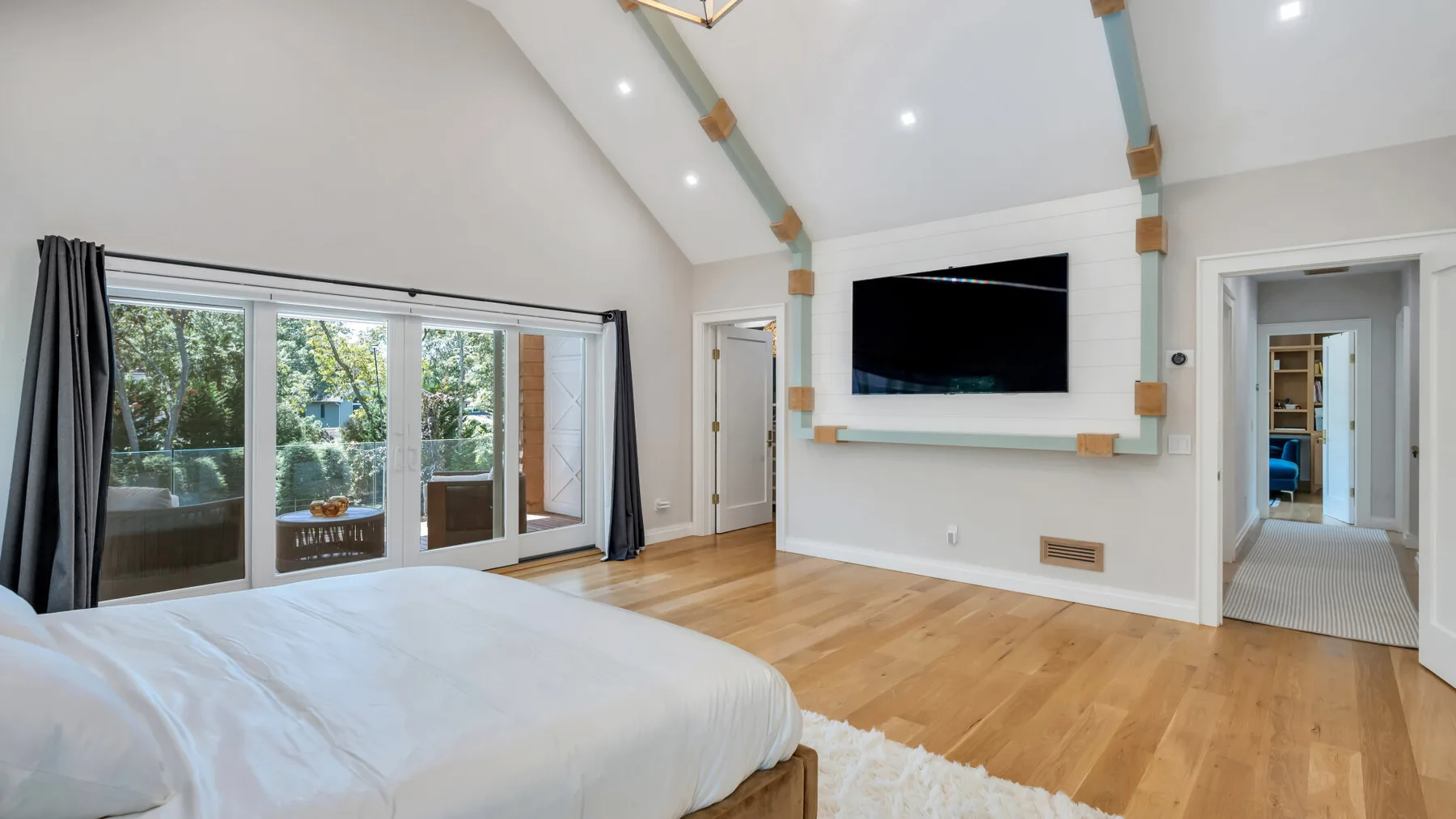 A bright bedroom with a large bed, glass doors, and a wall-mounted television.