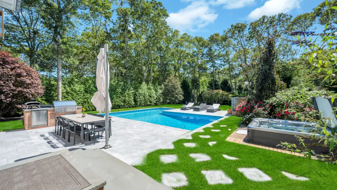An outdoor pool area with patio seating and a hot tub beside the lawn.