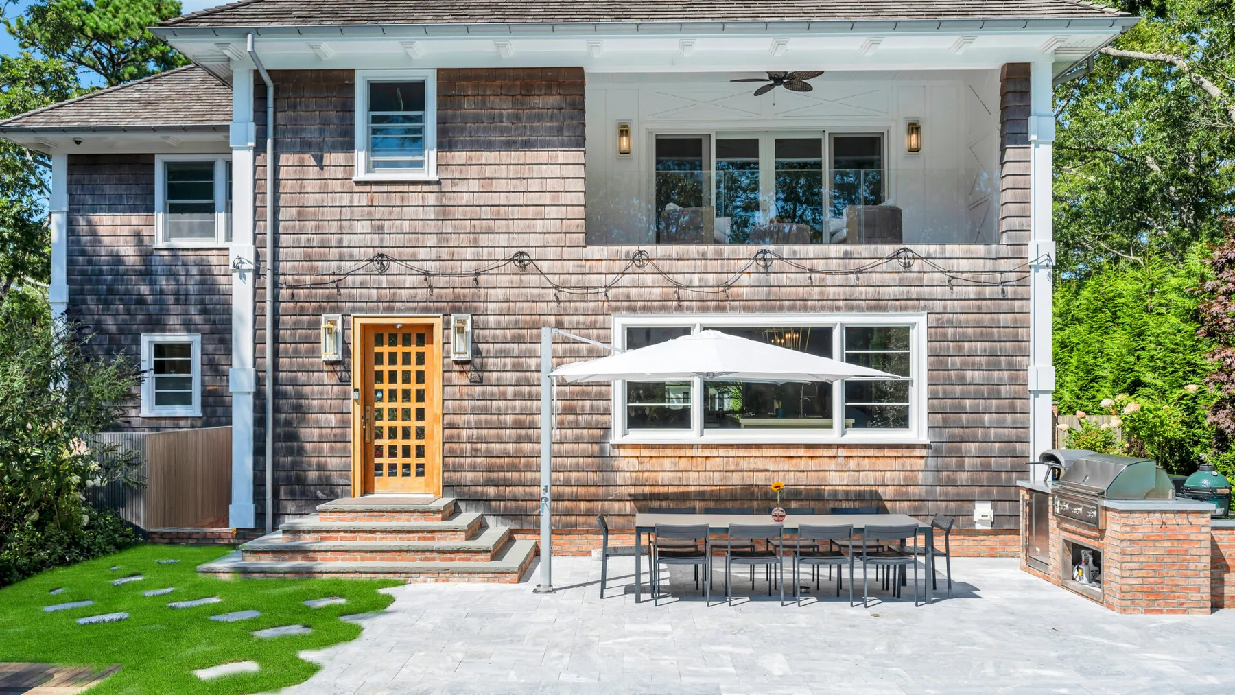 A house exterior with a patio dining area and a large white umbrella.